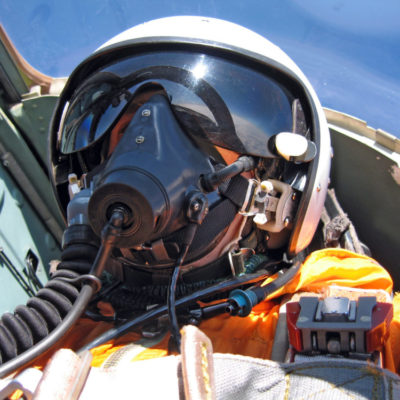 military pilot in the plane in a helmet in dark blue overalls against the blue sky